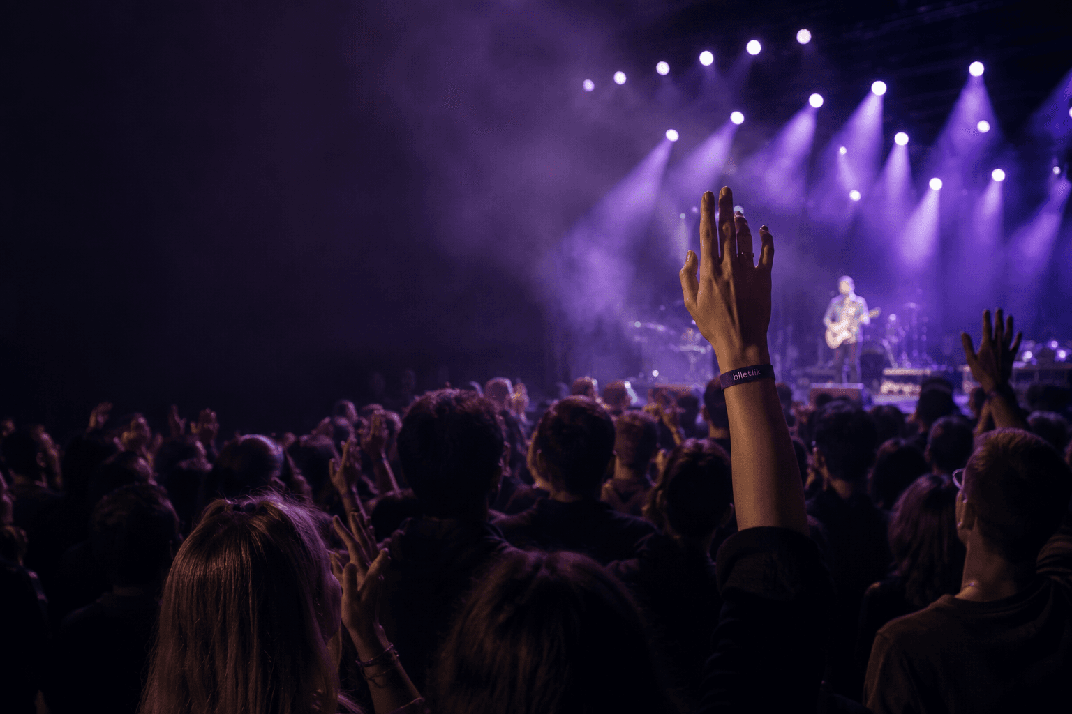 Canlı konserde sahneye uzanan eller ve biletlik bilekliği